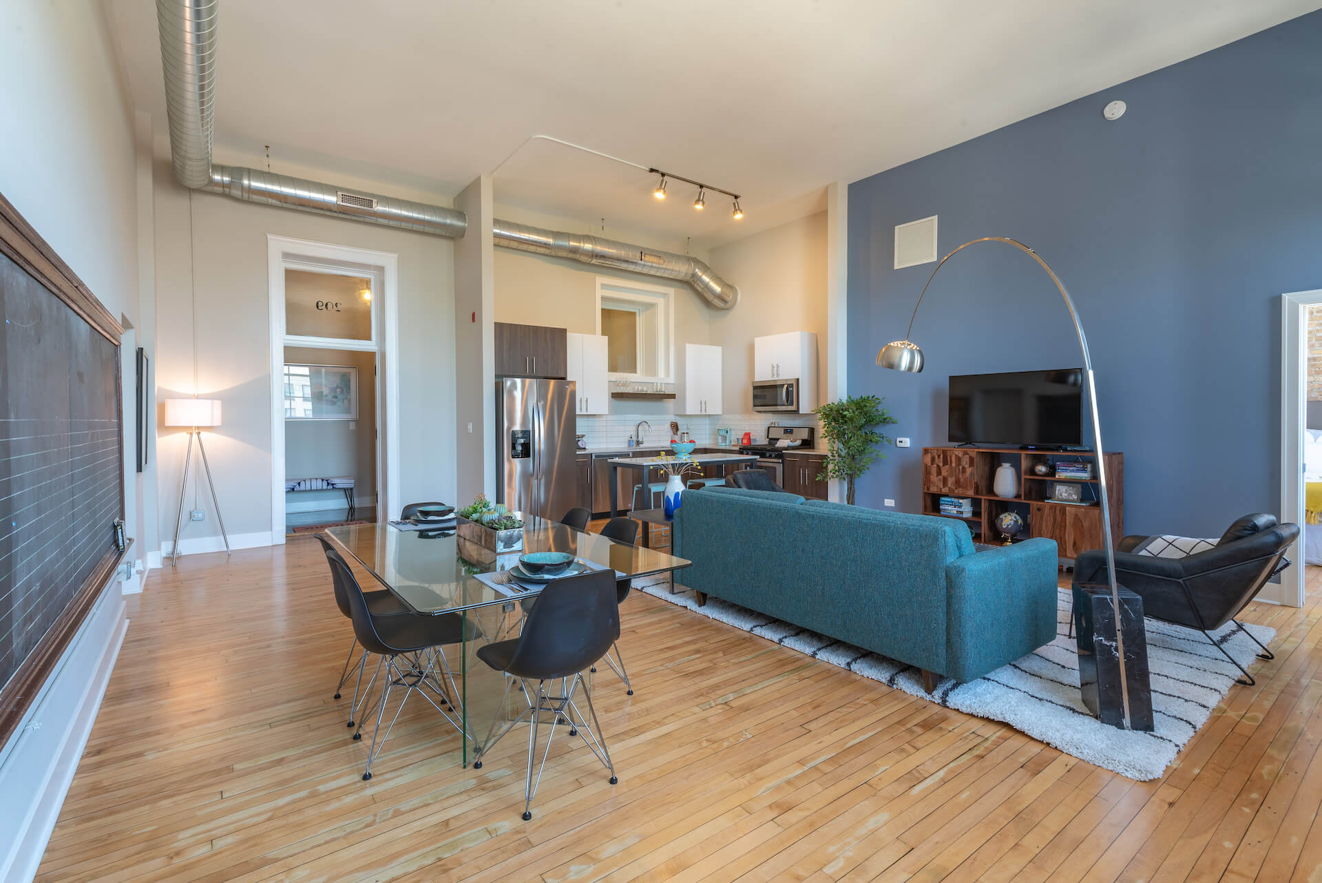 Open concept kitchen, living, and dining space with high ceiling and wood flooring.