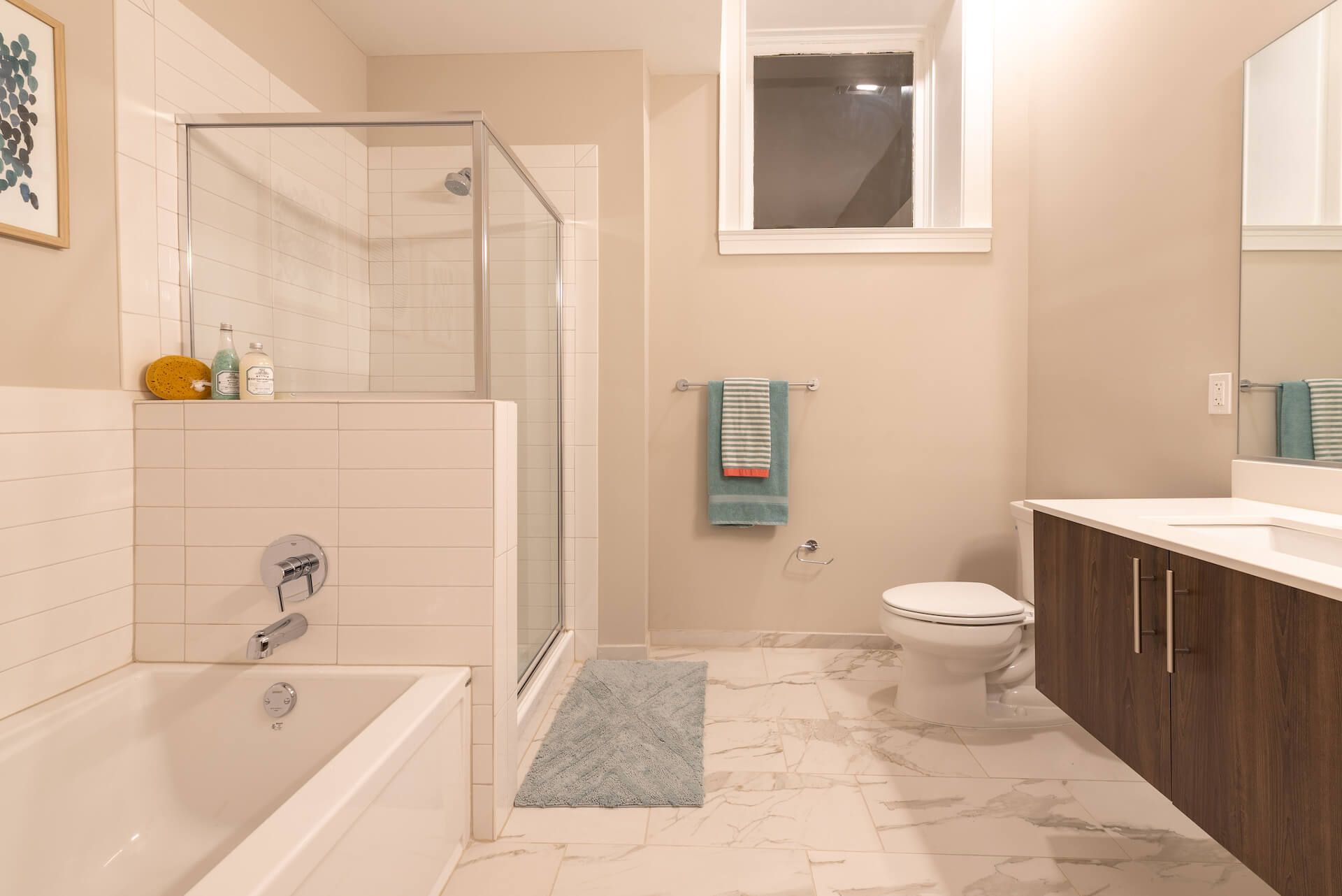 Spacious bathroom with custom vanity, bathtub, glass shower, and marble style tile.