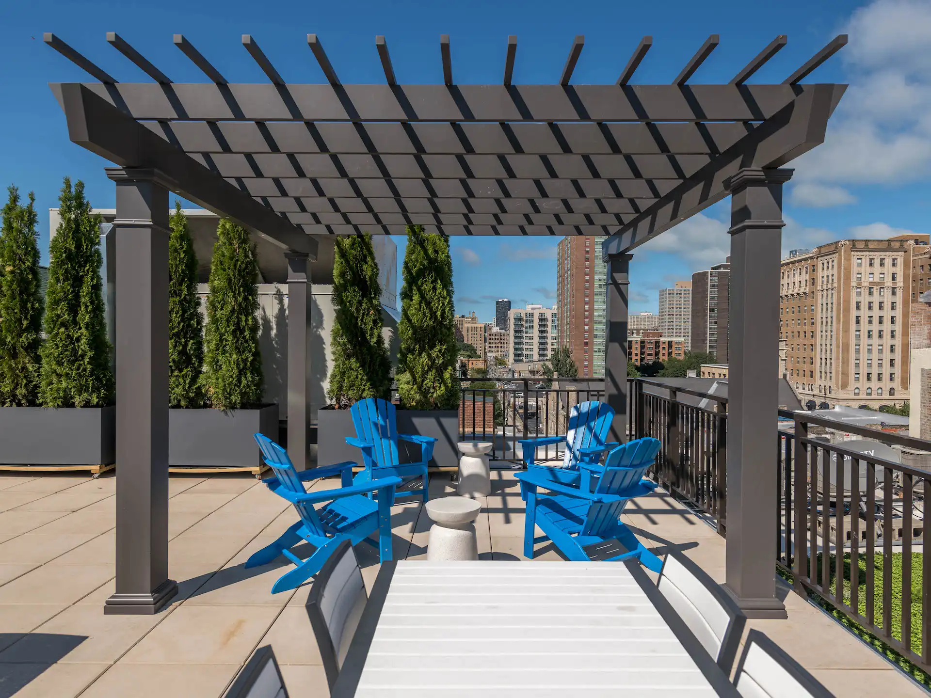 Rooftop patio with pergola and adirondack chairs and trees in planters.