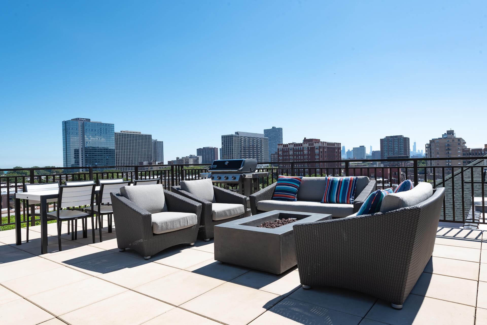 Rooftop patio with firepit and cushioned seating, six person table, and grill area with view of city skyline.