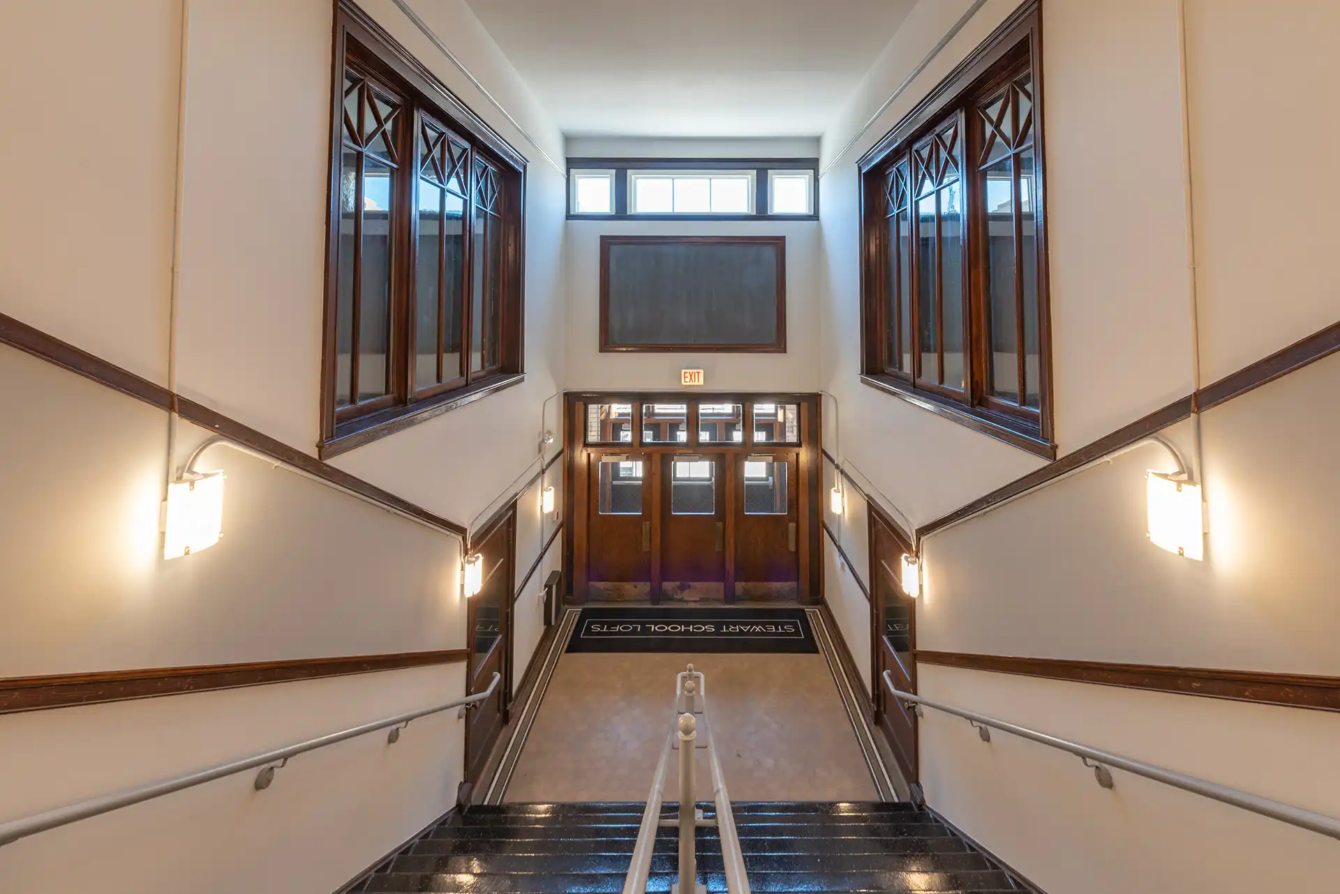 Stewart School Lofts lobby staircase with sconce lighting and dark wood framed windows.